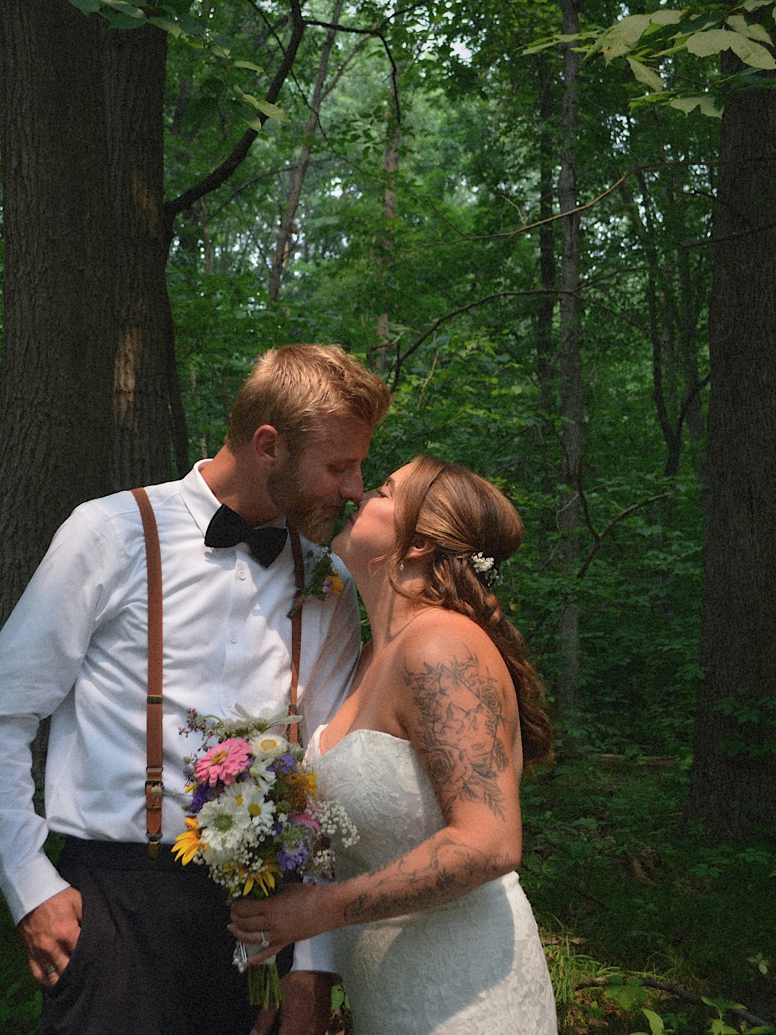 A newly married couple sharing a kiss in a green woodland